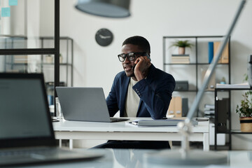 Aufkleber - Young confident male broker or agent talking to client on smartphone while sitting by workplace in front of laptop and analyzing data