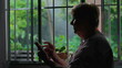 Silhouette of senior woman using modern technology at home. Elderly lady holding phone and scrolling internet online by winodw