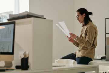 Aufkleber - Focus on young serious broker or accountant in eyeglasses looking through financial documents or new contract while sitting on desk