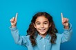 © Markus Schröder - Headshot portrait photography of a grinning kid female pointing with two hands and fingers to the side against a cerulean blue background. With generative AI technology