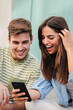 © Jose Calsina - Vertical portrait of two teenage happy friends watching funny videos browsing on internet app with a smartphone and smiling together. Caucasian couple using a cell phone to post in a social media