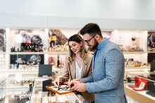 Elegant Middle Age Businessman Choosing And Buying His New Expensive Watch. Beautiful Young Female Seller Helps Him To Make Good Decision. Fashion Style And Elegance Concept.