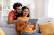 © Prostock-studio - Technologies For Leisure. Happy Indian Spouses Relaxing With Digital Tablet At Home