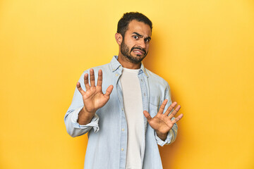 casual young latino man against a vibrant yellow studio background, rejecting someone showing a gest