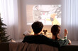 © New Africa - Couple watching romantic Christmas movie via video projector at home, back view