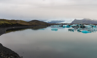 vue sur une baie avec des gros morceaux de glace flottant au loin lors d'une journée avec le nuages bas d'été