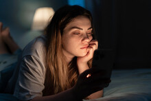 Addicted Young Woman Chatting And Surfing On The Internet With Smartphone Late At Night In Bed. Insomnia And Mobile Addiction