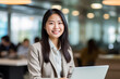 © Surachetsh - A charming young Asian woman wearing elegant beige outfit sits in indoor cafe, flashing a warm smile as she diligently works on laptop, creating professional and inviting atmosphere. generative AI.