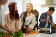 © DragonImages - Happy young Asian woman in casualwear talking to her friends in the kitchen while chopping fresh vegetables and preparing dinner