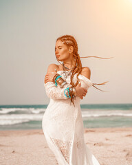 Wall Mural - Model in boho style in a white long dress and silver jewelry on the beach. Her hair is braided, and there are many bracelets on her arms.