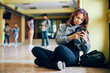 © Drazen - Pensive teenage girl texting on cell phone in hallway at high school.