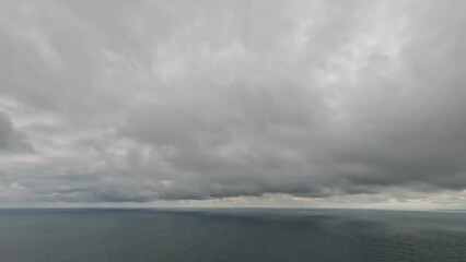 Wall Mural - Timelapse of dark rain clouds moving in overcast grey sky over a sea horizon during bad weather. Abstract aerial nature ocean sunset sea and sky. Rainy weather. Climate change, global warming concept
