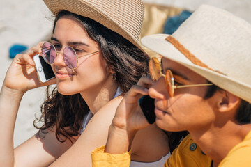 young couple on the beach sitting talking with mobile phone