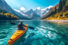 A Dynamic Photo Of An Individual Kayaking On A Serene Blue Lake, Surrounded By Majestic Mountains.