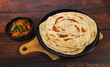 Kerala Parathas or Porotta Roti with red spicy chilly chicken. Barotta naan is a layered flatbread made from maida whole wheat flour. Indian food on a wooden table.