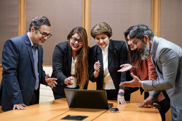 Indian corporate woman presenting project information to other businesspeople or employee, using laptop at meeting hall.