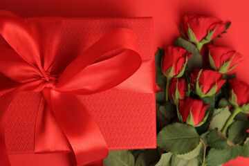 Beautiful gift box with bow and roses on red background, flat lay