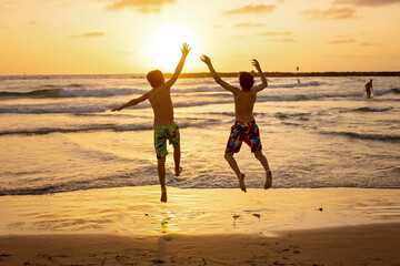 Poster - Happy teenager boys, running and playing on the beach on sunset, splashing water and jumping on the sand