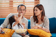 © Kiattisak - Asian Family consisting of parents, happy daughter watching TV or movie eating popcorn on sofa in living room at home. enjoy relaxing happiness.