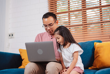 Cute little asian daughter with father working on laptop at home. single loving dad man shopping insurance to daughter by online technology.