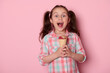 Studio portrait on pink background of a beautiful mischievous Caucasian little kid girl with a tasty ice cream in waffle cone, expressing happiness, surprise and positive emotions, looking at camera