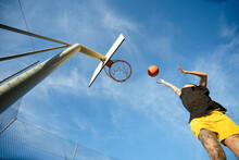 Basketball Player Throwing Ball Into Basket Against Blue Sky