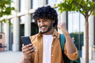 young hispanic student celebrating victory and happy good news online, man reading page interent rec