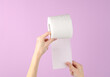 Hands holding roll of white toilet paper on purple background