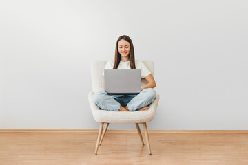 full length portrait of a happy woman holding laptop computer while sitting on a chair