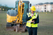 © Olena - Construction manager in suit and helmet at a construction site. Construction manager worker or supervisor wearing hardhat in front of house. Supervisor construction manager near excavator. Renovation.
