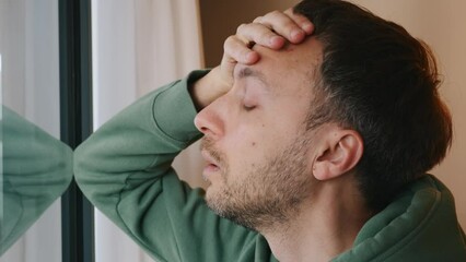 Wall Mural - Depressed man standing alone near window with stressed and worried problem face. Mental health and middle-age crisis concept.