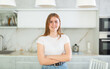 © JackF - Portrait of positive girl teenager in casual wear smiling at camera while standing with crossed hands in cozy kitchen