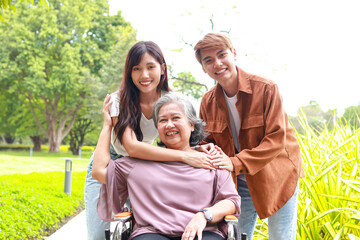 Family concept. Daughter and son bring elderly mother in wheelchair to breathe fresh air at outdoor park. elderly health care