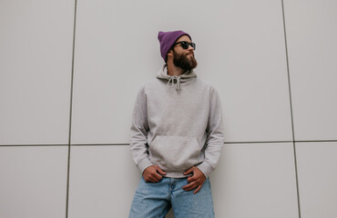 city portrait of handsome hipster guy with beard wearing gray blank hoodie or sweatshirt and hat wit