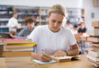 © JackF - Fifteen-year-old girl studying in the library writes out an important synopsis from a textbook