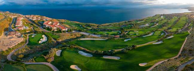 Residential community with a golf course overlooking the ocean under cloudy skies