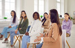 © Studio Romantic - Diverse women gathered together listening business coach at seminar. Multiracial young woman sitting on chairs during corporate staff training, group therapy session in office