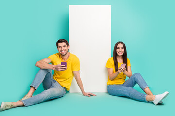 Sticker - Photo of cheerful pretty married couple wear yellow t-shirts writing sms gadget empty space isolated teal color background