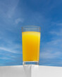 Glass of freshly squeezed orange juice. Trendy Hero View.  Delicious refreshing summer drink in a glass on podium. Sunshine, background blue sky. 