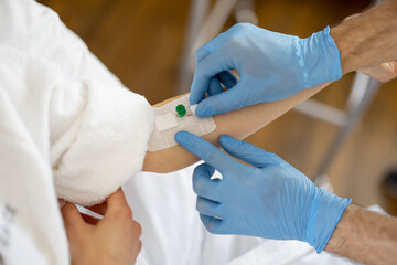 Nurse inserts catheter for injections into the arm of young patient in medical ward, close-up Concept of medical procedures