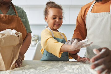 Wall Mural - African American little girl using flour to bake pastry together with her parents