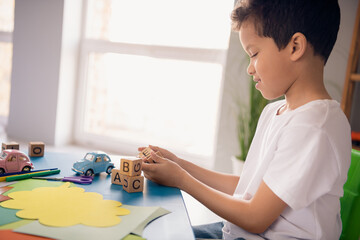 Wall Mural - Photo of charming smiling small boy wear white t-shirt sitting table collecting letters indoors room home house