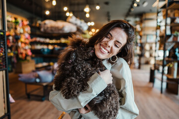 Beautiful and happy young woman sitting in modern pet shop cafe bar and enjoying in fresh coffee together with her adorable brown toy poodle.