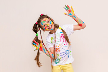 Wall Mural - A little schoolgirl with painted hands and face with multicolored paints. A girl stained with paints. The concept of children's creativity. Funny child draws with his hands.