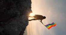 LGBTQ Community Rainbow Flag. A Symbolic Moment Of A Woman Proudly Standing At The Top Of The Mountain And Waving Rainbow Flag. Concept Of Human Rights, Freedom And Equality