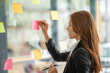 © Wuttichaik - Happy businesswoman planning ideas project work on a glass of wall with colorful memo