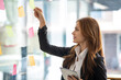 © Wuttichaik - Happy businesswoman planning ideas project work on a glass of wall with colorful memo