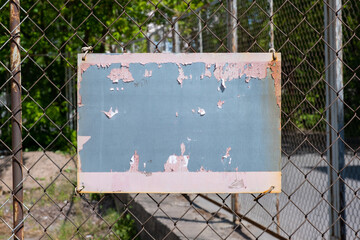 An empty old sign on a chain link fence