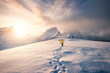 Leinwandbild Motiv Mountaineer walking with footprint in snow storm and sunrise over snowy mountain in Senja Island