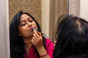 Wall Mural - Beautiful Asian woman front of mirror applying make up lips with lipstick at bed room.